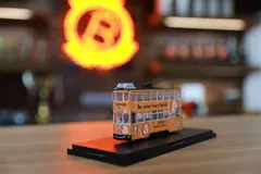 Photo of an orange model tram on a black display base, with a glowing orange bitcoin sign blurred behind it.