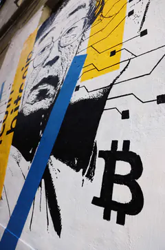 Angled photo of a street mural showing part of a face, yellow and blue stripes, circuit lines and a black bitcoin symbol.
